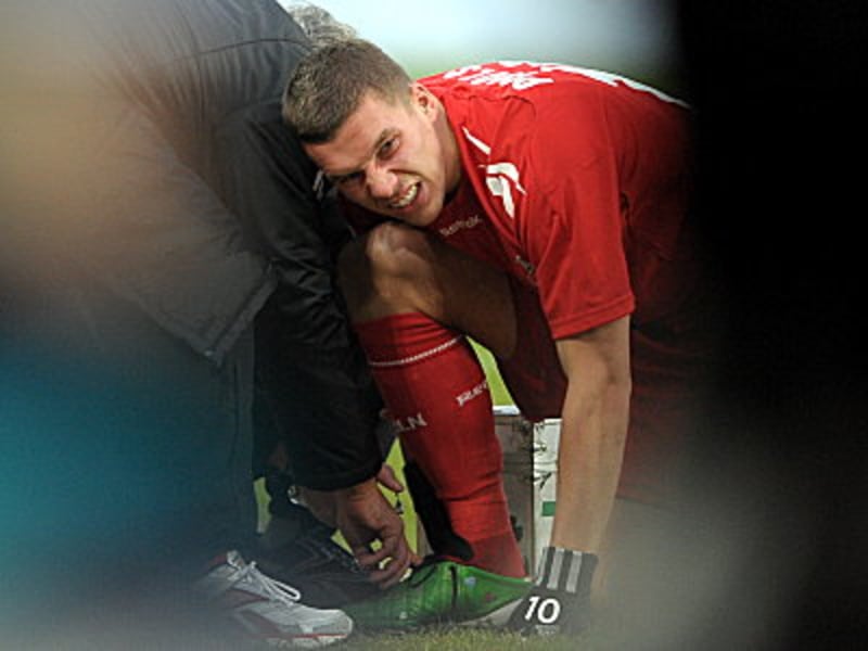 Die Schmerzen im Gesicht: Podolskis angeschlagener Kn&#246;chel wird verarztet.