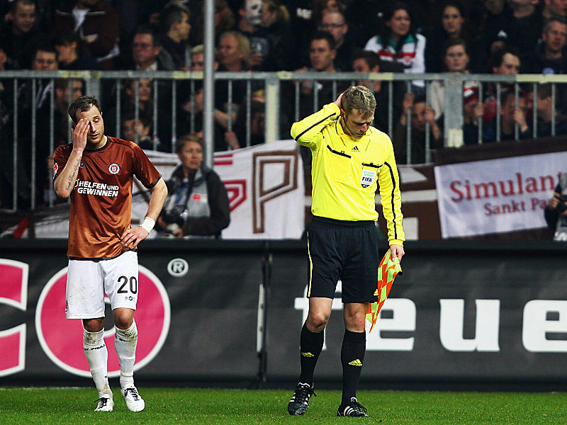 Schreckensmoment: Assistent Thorsten Schiffner (re.) hält sich am Kopf, nachdem er von einem vollen Bierbecher am Kopf getroffen wurde. St. Paulis Lehmann ahnt Böses.