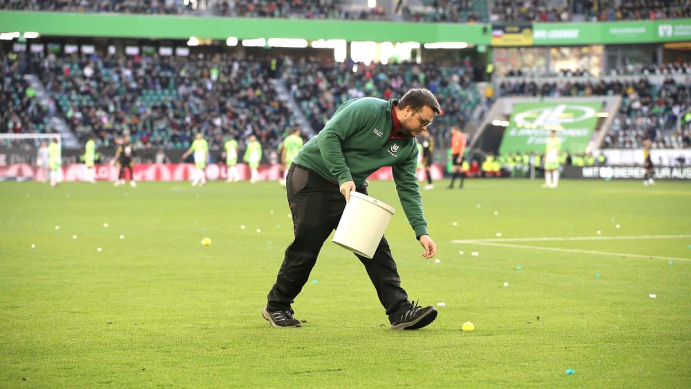 Sammeln für den guten Zweck: Ein Helfer des VfL Wolfsburg hebt einen Tennisball auf.