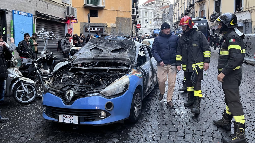 Schadensbegutachtung: Feuerwehrleute schauen sich ein abgebranntes Polizeiauto an.