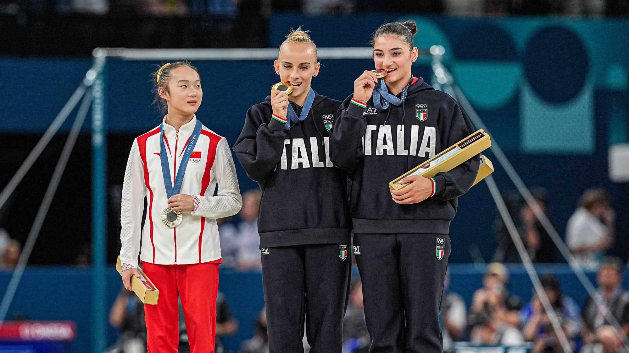 Yaqin Zhou (China) beobachtet ihre Turnkolleginnen Alice D'Amato und Manila Esposito (beide Italien) beim Medaillen-Bisstest