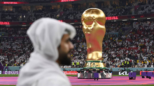 Ein Katarer steht vor einem riesigen WM-Pokal, der vor Anpfiff auf dem Spielfeld steht.